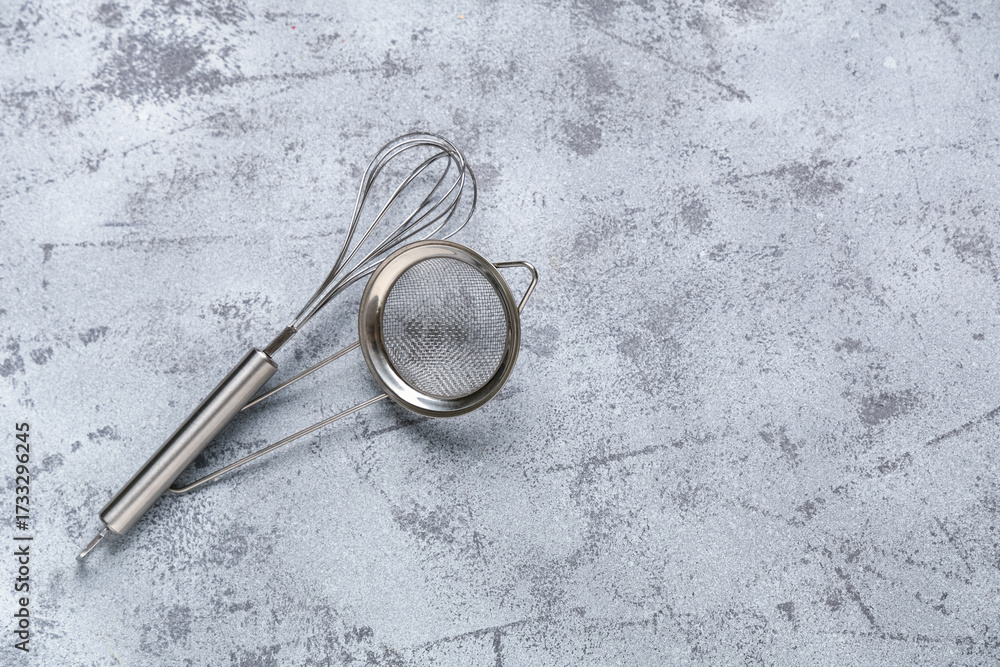 Fototapeta premium Metal sieve with whisk on grey grunge background