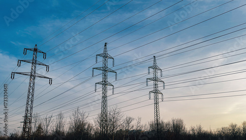 Electric power transmission towers and cables silhouetted against a blue and cloudy sky.