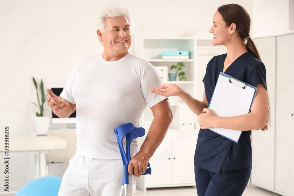 Obraz premium Female therapist and senior man with crutches in rehabilitation center