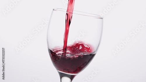 Red wine slowly pouring in glass over white background. Close-up of red wine forms beautiful wave in glass. Grape wine pouring in glass at white background. 4k footage.