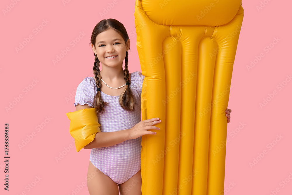 Obraz premium Cute little girl in swimsuit with inflatable armbands and mattress on pink background