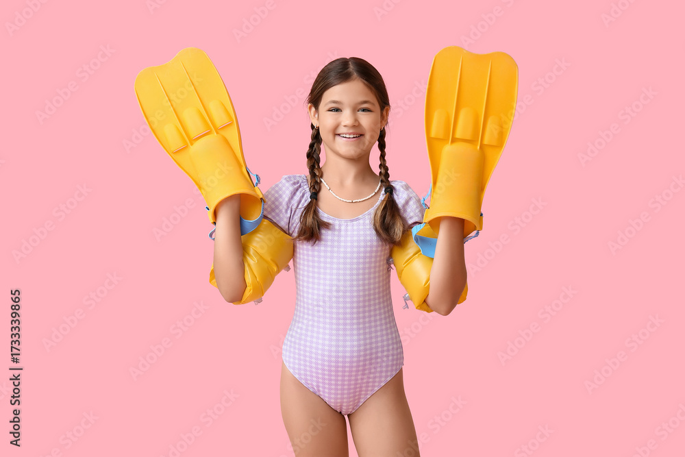 Φωτογραφία Cute little girl in swimsuit with inflatable armbands and flippers on pink backg