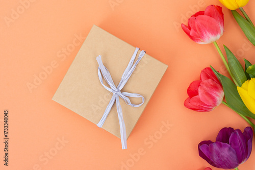 National Cartonnage Day. Colorful Tulips Surrounding a Wrapped Gift on a Peach Background