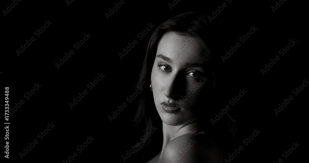Fototapeta premium Black and white portrait of beautiful model posing in studio with bare shoulders and dark background, creating a dramatic and evocative image