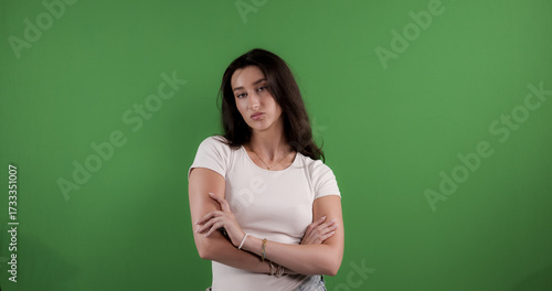 Tableau sur toile Young woman posing with crossed arms on green screen background, expressing disa