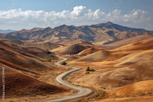 Winding road through brown hills mountains in background scattered trees partly cloudy sky
