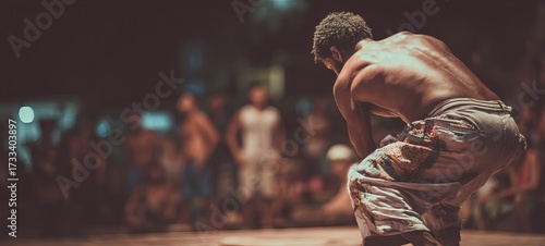 A man performs a dance in a dimly lit outdoor setting.  Many onlookers are blurred in the background
