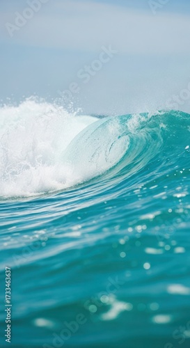 A close-up view of a powerful wave cresting, showcasing its translucent turquoise water and foamy white top against a clear sky.