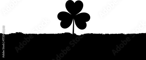Bold black shamrock silhouette emerges from textured ground against stark white backdrop, symbolizing luck and nature's simple elegance.