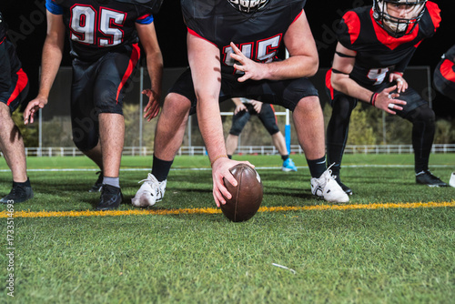 Fotografie American football players in uniform lining up on the green turf, hands on knees