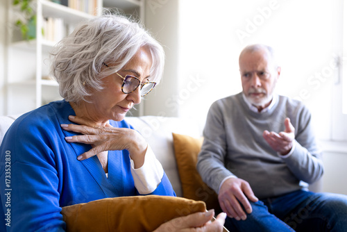 Senior woman feeling sad while senior man is talking to her on the sofa at home
