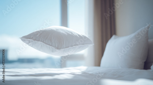 Floating white pillow above a neatly made bed in a bright room
