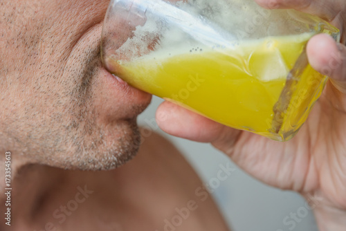 Closeup photo of young man drinking meal replacement protein cocktail. Healthy adult drinking yellow protein mix, close-up lips and glass