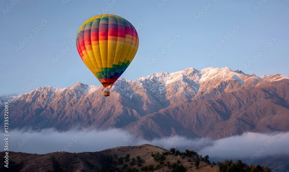 Fototapeta premium hot air balloon floating above snowy mountain range at sunrise