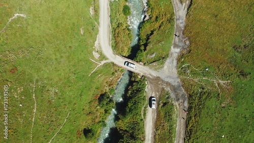 A top-down aerial view of the travelers' car driving across the bridge over a mountain river.