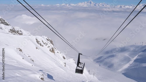 Ski lift gondola ascending snow covered mountain. Alpine landscape with mont blanc massif visible above thick sea of clouds. Mountain ski resort. Powerful cables lift gondola cabin to top of mountain