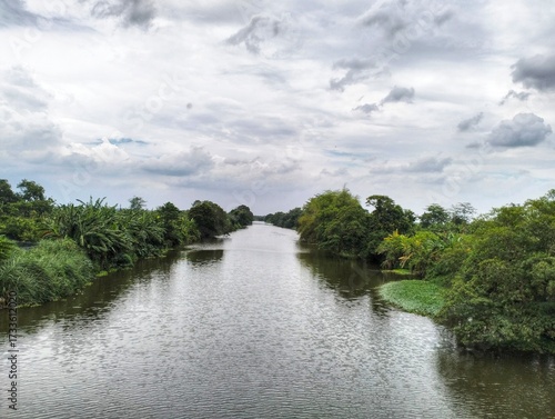 A calm river stretches between green trees with a cloudy sky above.
