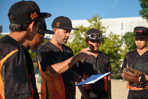 Coach explaining game strategy on a clipboard to his youth baseball team during practice