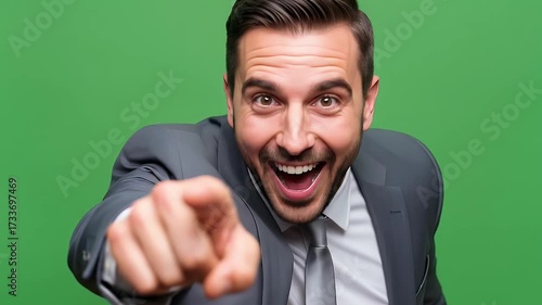 Excited businessman pointing forward in suit bright laughing on a green background with studio lighting showcasing positive emotion and anticipation