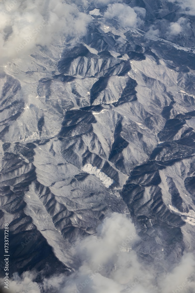 Obraz premium Aerial View of Rugged Mountain Ranges and Valleys Through Airplane Window with Dramatic Clouds