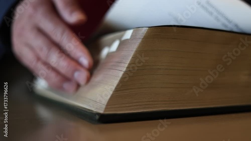 hand flipping pages of thick dictionary book on library desk. Concept of education, research, knowledge, study, learning resource, language reference, academic information access.