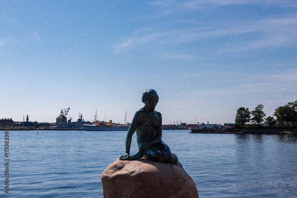 Obraz premium Copenhagen, Denmark 07-20-2025 The bronze statue of the Little Mermaid sitting on a rock by the waterside at the Langelinie promenade in Copenhagen. The small and unimposing statue is an icon in town.