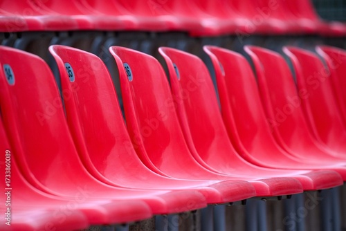 Close view of empty red plastic stadium seats in a single curved row, numbers visible. Repetition and shallow depth of field create a clean abstract sports-venue pattern.