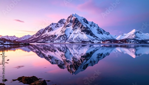 Fototapeta Naklejka Na Ścianę i Meble -  A serene winter landscape showcases snow-capped mountains reflected perfectly in a tranquil lake, bathed in the vibrant hues of a sunrise.