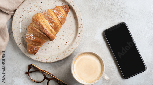 Top down breakfast flat lay: croissant, latte, smartphone, on neutral tabletop, plenty of negative space for text