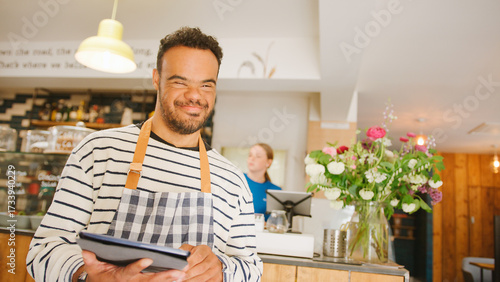 Portrait Of Man With Down Syndrome Working In Food Shop Using Digital Tablet