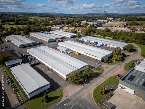 Modern warehouse and distribution depot seen from above with metal cladding, parking bays and surrounding trees in industrial estate on bright sunny day