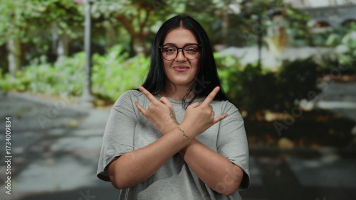 Valokuva Woman smiling while making rock gesture with hands in outdoor park setting showcasing confidence and positivity with trees in background