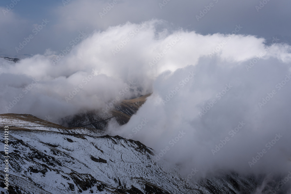 Fototapeta premium Dramatic high mountain landscape with snow, rocks and low clouds