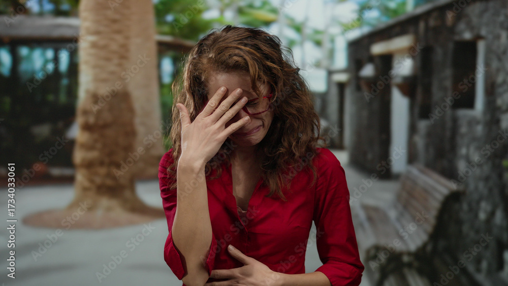 Fototapeta premium Woman crying in city street outdoor wearing red glasses and shirt with brown hair expressing sadness and emotion in urban daytime setting