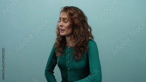 Woman experiencing stomach pain on blue background looks uncomfortable in isolation, capturing a moment of distress and health concern.