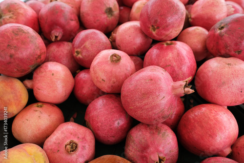 Fresh pomegranates and peaches arranged on a black plastic crate, likely at a market or fruit stand.