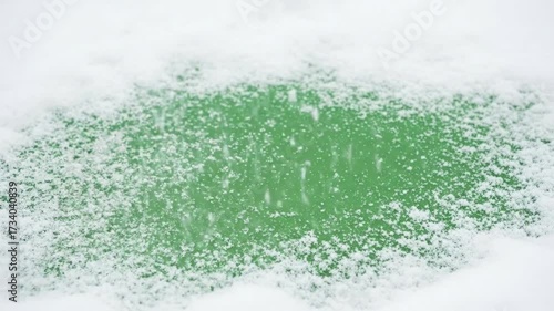 White snowflakes fall and accumulate on a vibrant green background creating a wintry abstract pattern