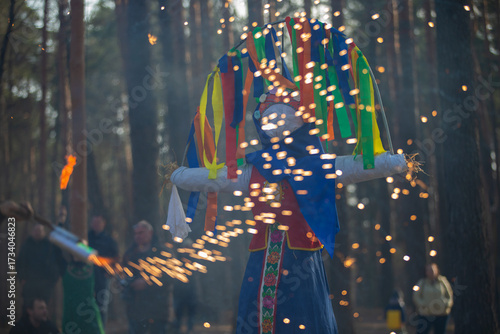 Celebration of a traditional festival with a colorful effigy surrounded by sparklers in a forest setting during daytime