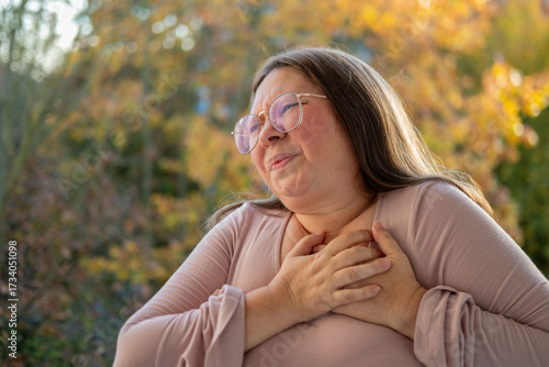 Middle-aged woman experiencing chest pain, pressing hands to heart. Concept of health problems, cardiac arrest, and distress, Health risk, heart failure, and emergency situation