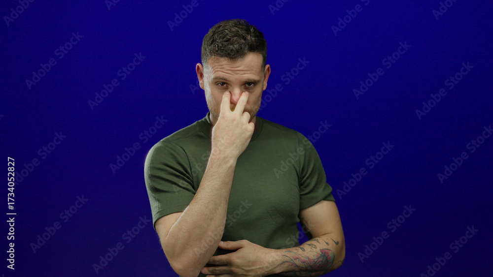 © Krakenimages.com - Young hispanic man making watch gesture with fingers over isolated blue background, wearing casual green shirt, looking serious and confident in the gesture captured.