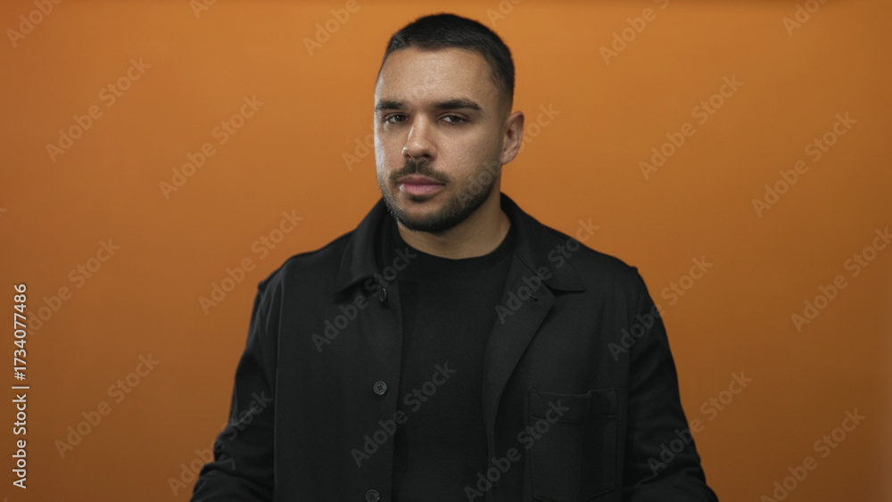 Obraz premium Man extends hands with open palms and holds a thoughtful gaze in orange studio setting; calm reflection and focus.