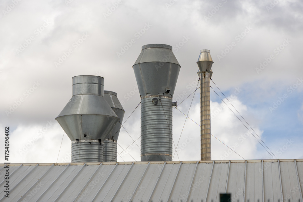 Obraz premium Industrial exhaust pipes rising from metal roof into cloudy sky