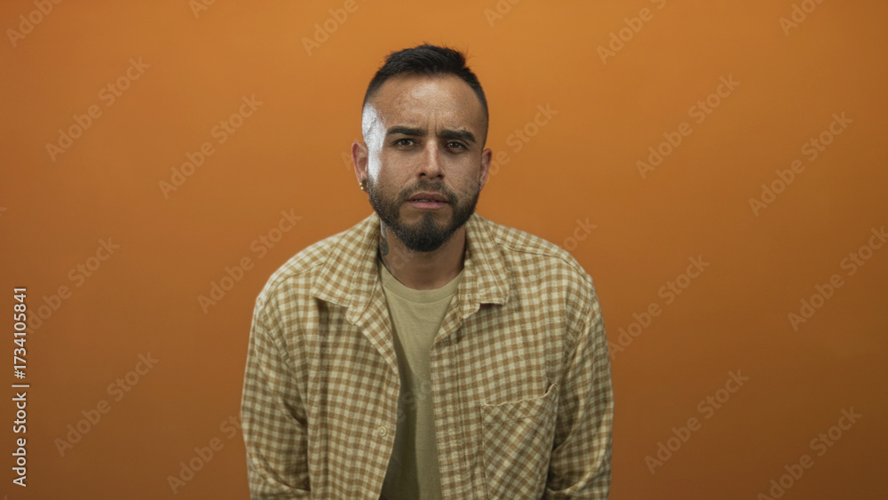 Obraz premium Man frowning with visible face and beard, leaning slightly forward in an orange studio; introspection.