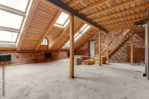 Spacious attic with exposed brick walls, wooden beams and large skylight windows under sloped ceiling