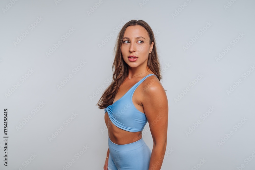 Fototapeta premium Woman in light blue activewear posing against a plain backdrop during a fitness photoshoot