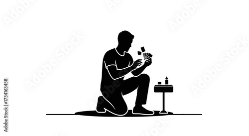 Focused man playing cards on floor, a candle glows on nearby table, evoking solitude and concentration.