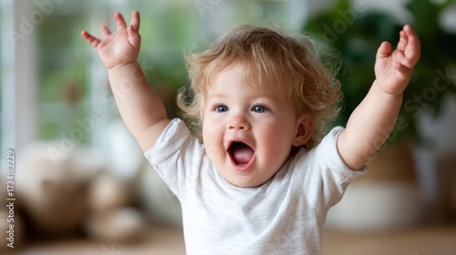 A joyful baby with curly blonde hair raises their arms in sheer delight, capturing the essence of carefree childhood and exuberant happiness in this beautifully lit image.