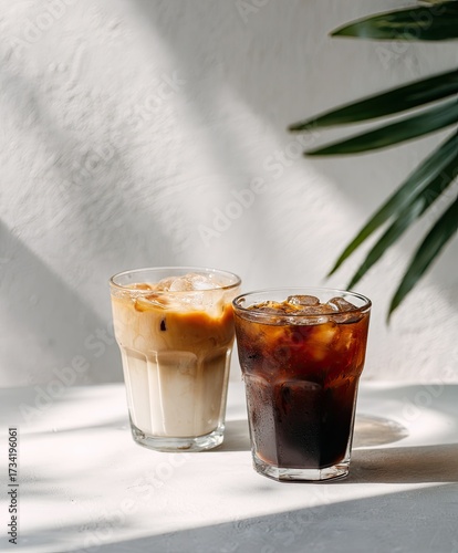 Two iced coffee drinks, one latte, one black, on a white surface, with sunlight