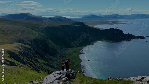 Wallpaper Mural Two hikers on a rocky outcrop overlook the stunning coastal landscape of Matind Andoy, Norway. The vibrant scenery showcases lush greenery and tranquil waters under a clear blue sky. Torontodigital.ca