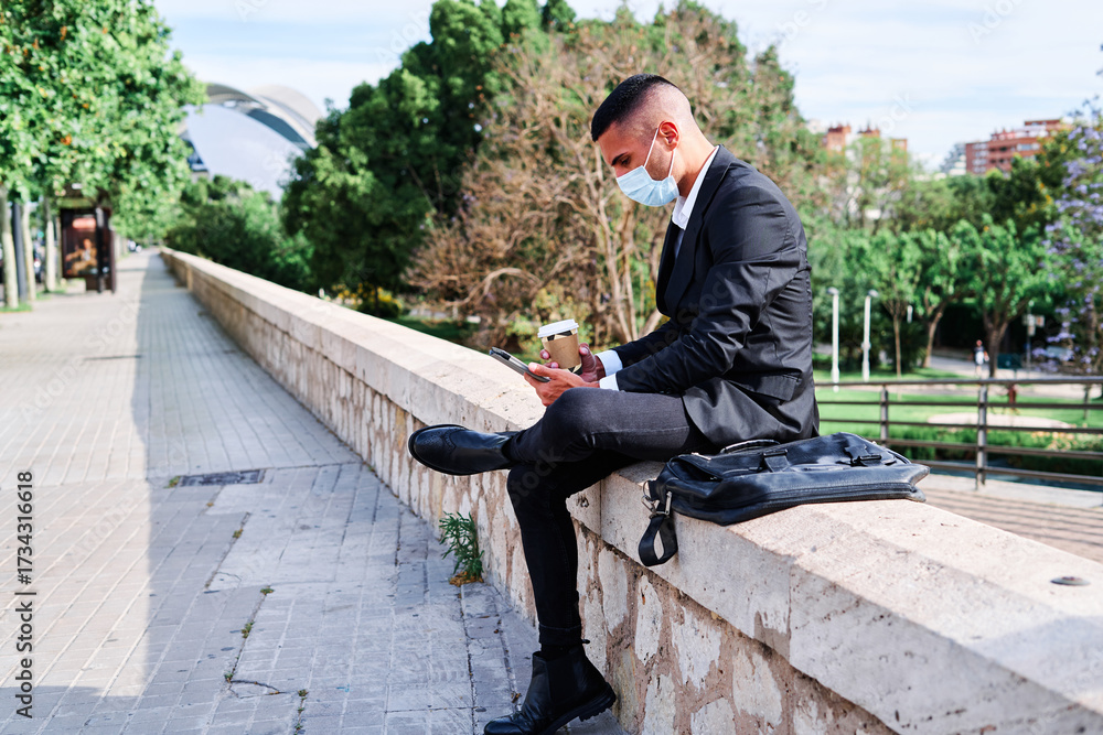 Obraz premium Businessman in suit checking phone at park with coffee during sunny day